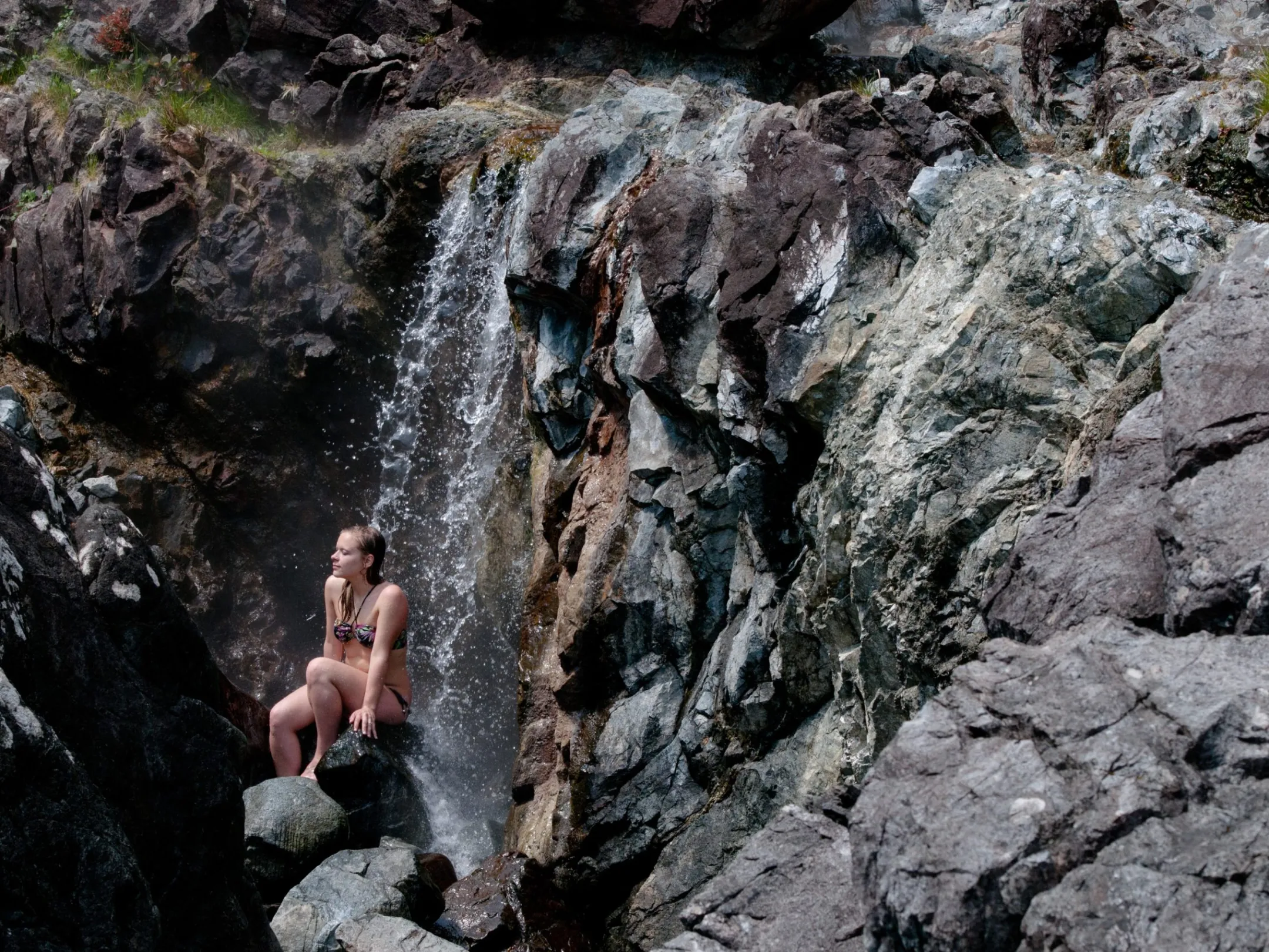 lady sits under waterfall at hot springs cove