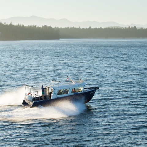 Boat speeding on a vast lake with forested hills in the background.